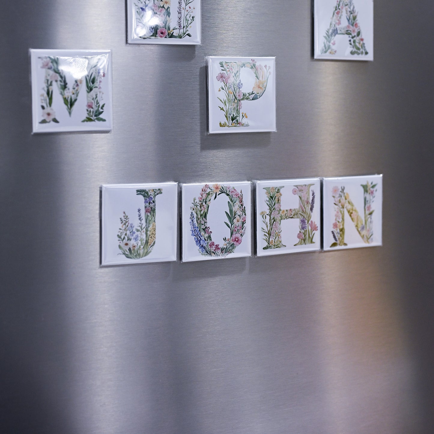 Floral letter magnets spelling 'JOHN' on a metallic surface