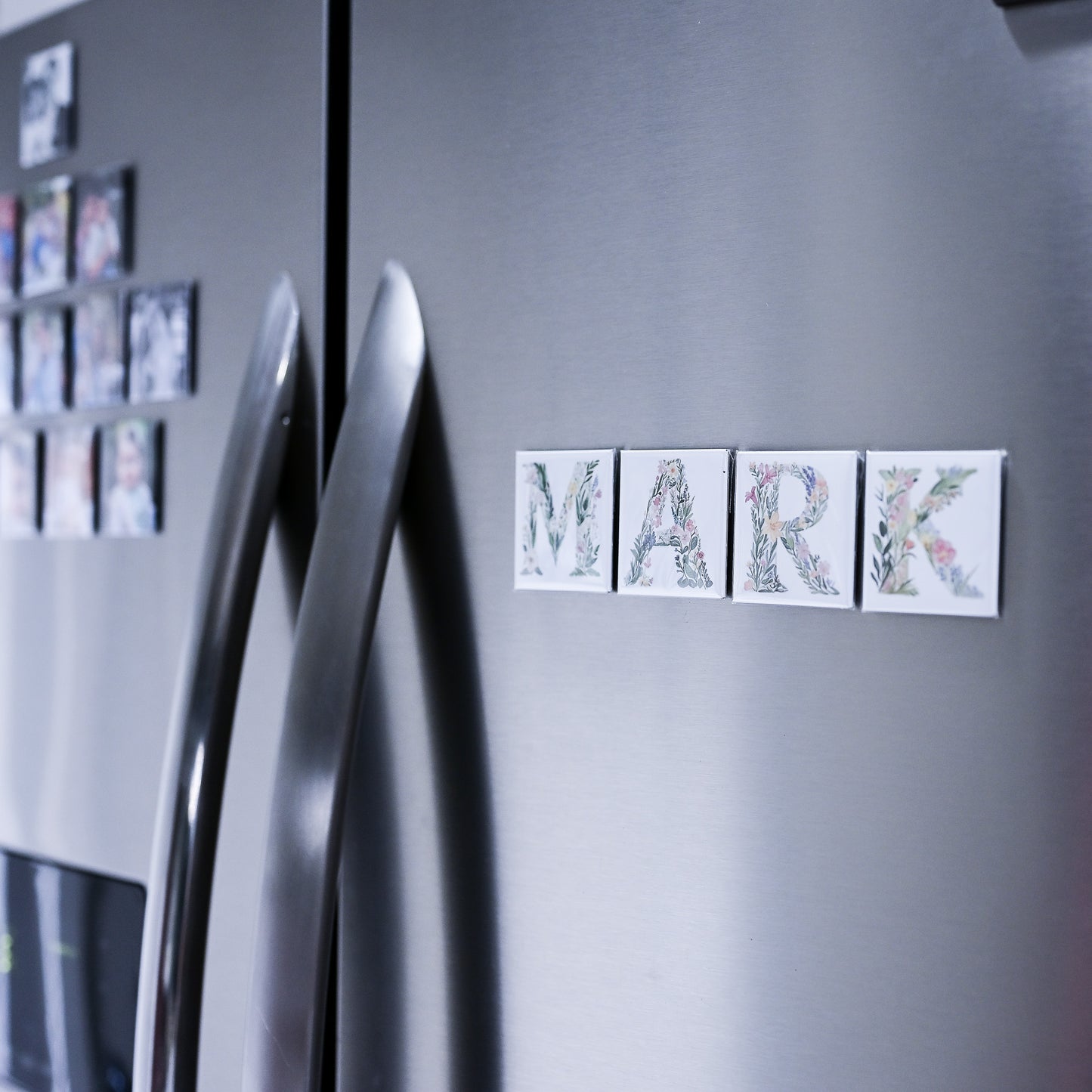 Silver refrigerator with decorative magnets spelling 'MARK' on a gray background