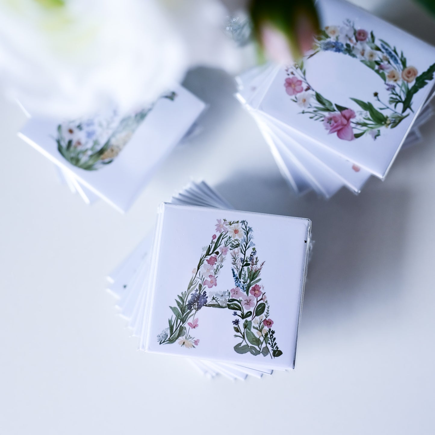 Stacks of fridge magnets with floral letter designs on a light surface