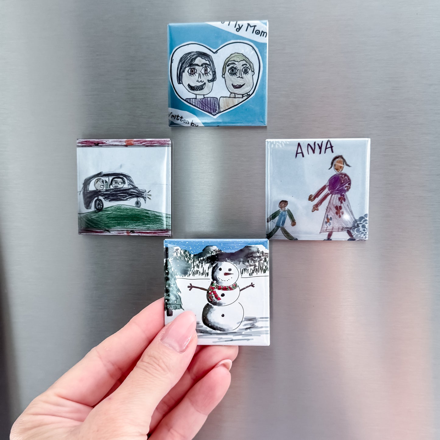 Collection of small photo magnets on a metallic surface showing kids art