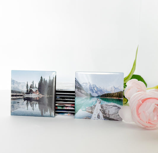 Set of photo magnets with mountain and lake scenes on a white surface with a pink flower.