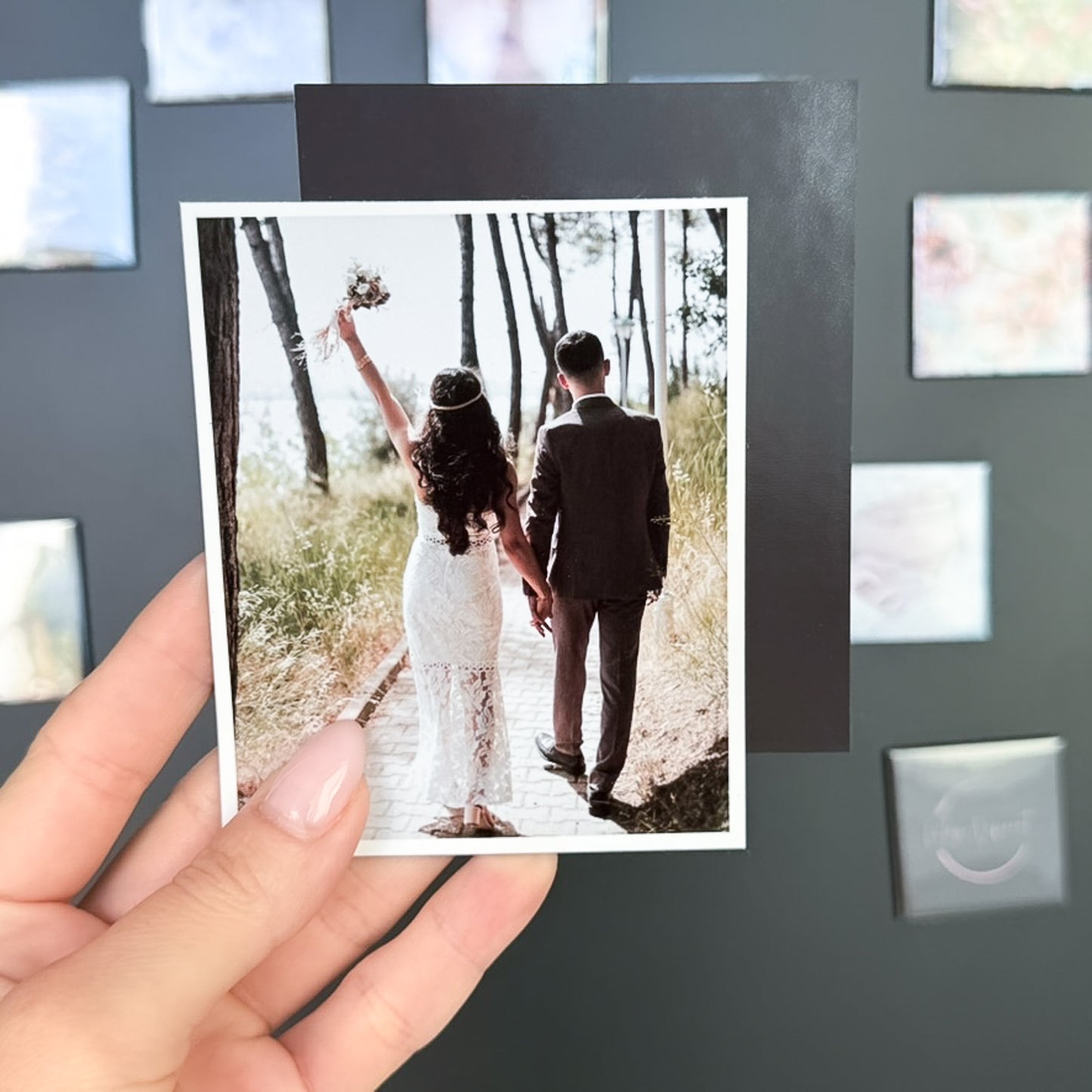 Hand holding a photo magnet of a couple walking together in a forest.