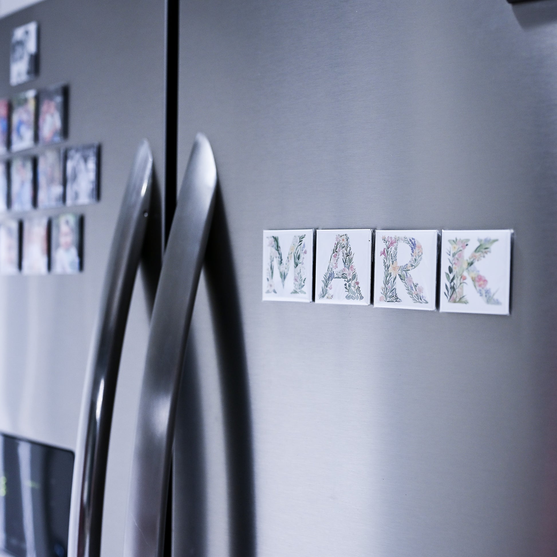 Silver refrigerator with decorative magnets spelling 'MARK' on a gray background