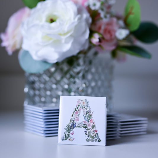Stack of fridge magnets with floral design and letter 'A' in front of a vase of flowers.