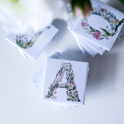 Stacks of fridge magnets with floral letter designs on a light surface