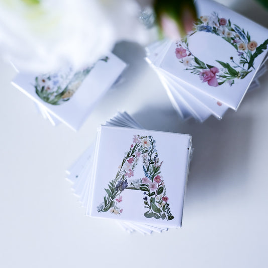 Stacks of fridge magnets with floral letter designs on a light surface