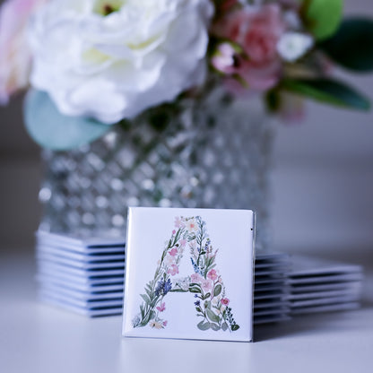 Stack of fridge magnets with floral letter 'A' design in front of a vase with flowers.
