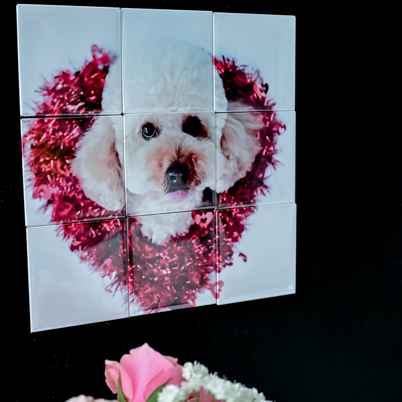 Collage of a dog with a heart-shaped wreath on a black background, with pink flowers in the foreground.