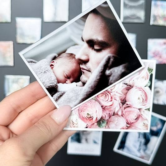 Hand holding a photo  magnet of a man and a baby with a floral design, against a background of other photo magnets.