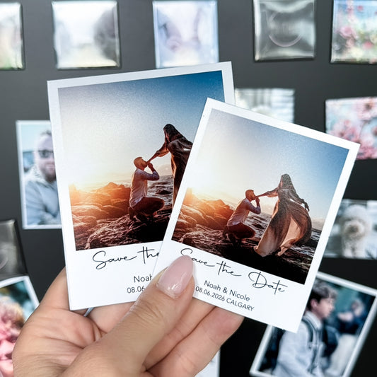 Two 'Save the Date' photo magnets  held by a hand with a blurred photo  magnet collage in the background.